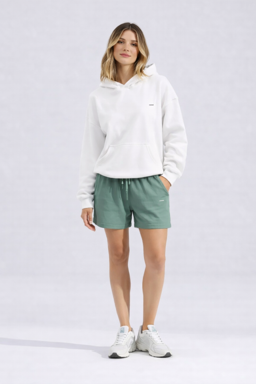 Hoodie femme blanc en coton biologique porté en studio avec un short vert et une allure décontractée