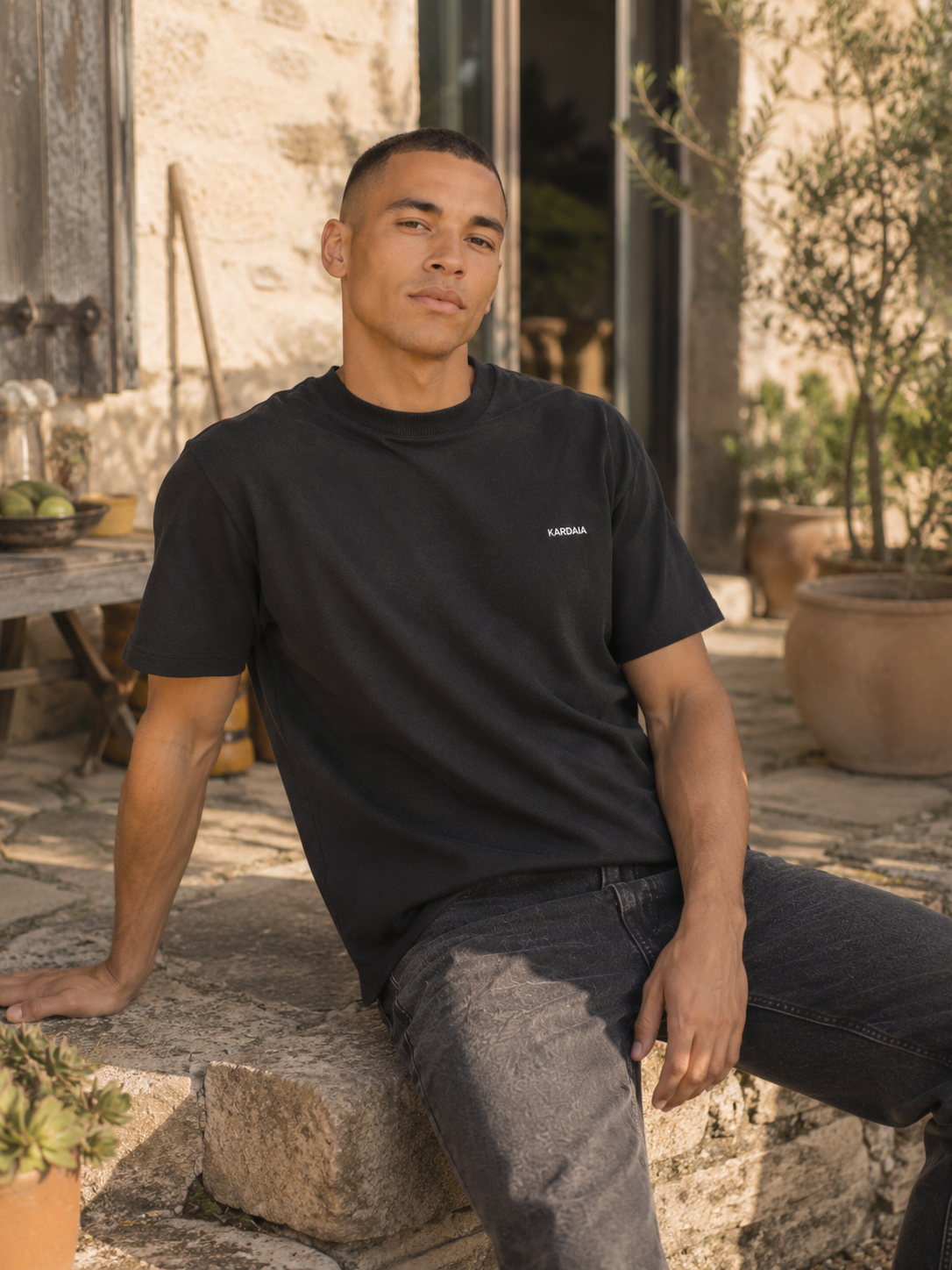 Homme assis sur un muret portant un t-shirt kardaia noir