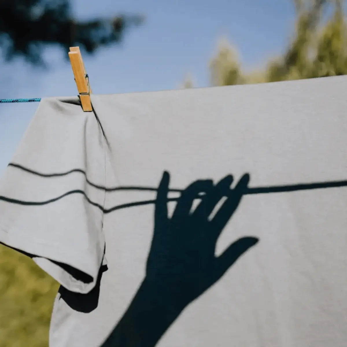 Ombre d'une main sur un t-shirt suspendu en plein air, lumière naturelle